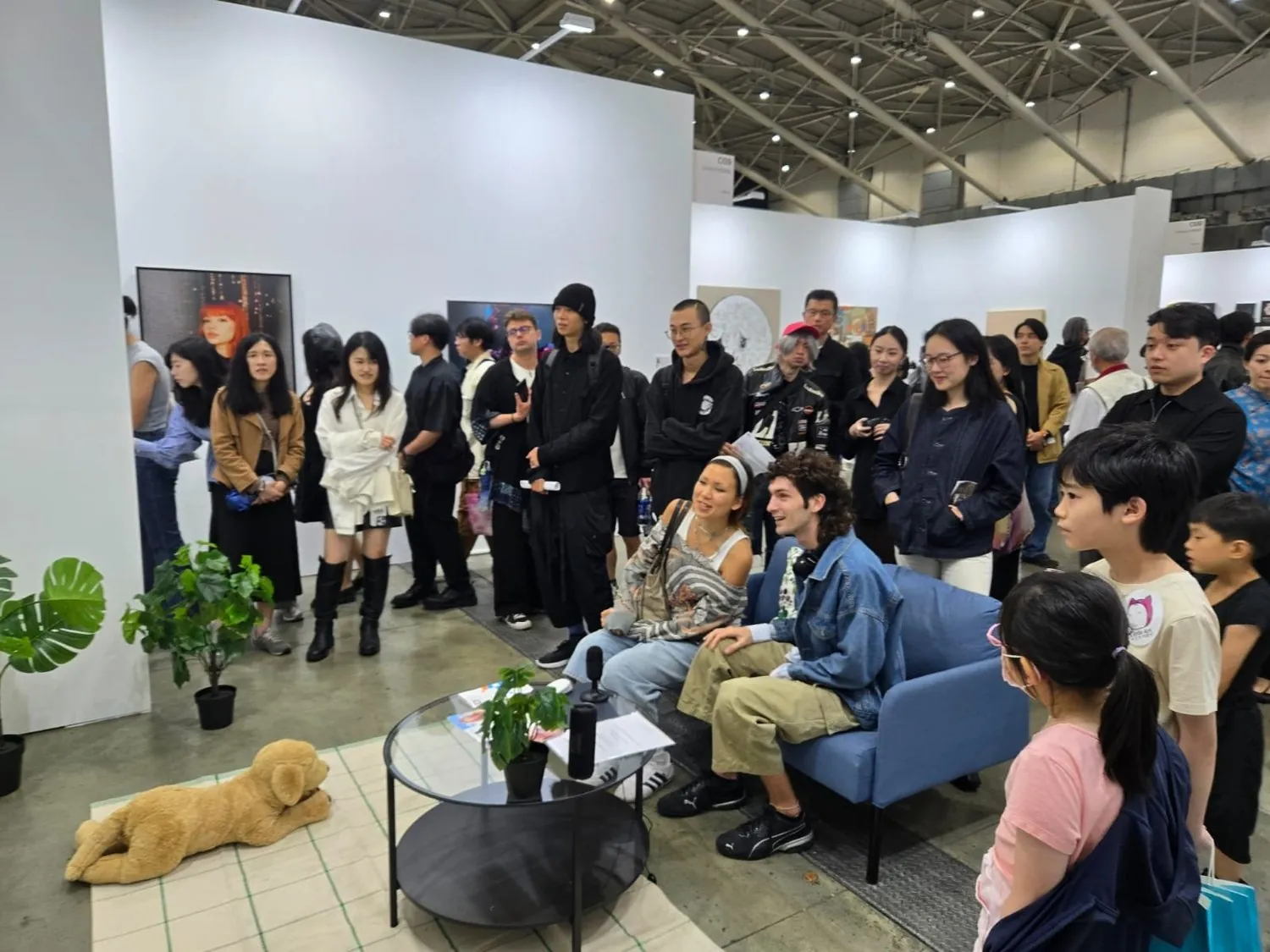 Large crowd engaging with Meet Eva Here at Taipei Dangdai 2025, inside a mock living room with artificial plants, a plush dog, and an AI companion on screen.